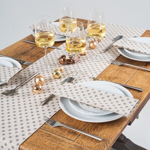 May include: A decorated dining table with champagne glasses, white plates, and star-patterned napkins. The wooden table is adorned with gold baubles and cutlery, creating a festive atmosphere.