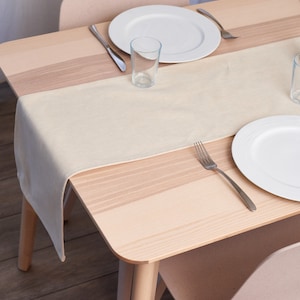 May include: A light beige table runner on a wooden table with two white plates, two glasses, and two forks. The table runner is made of a soft, textured fabric.