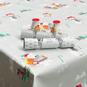 May include: A gray tablecloth with a festive Christmas design featuring snowmen, candy canes, and Christmas trees. There are silver and white Christmas crackers and two red and white ceramic salt and pepper shakers with gingerbread men designs.