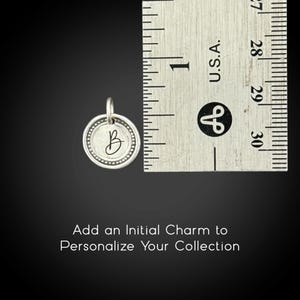 May include: A silver initial charm with the letter "B" inside a dotted circle, next to a ruler. The charm is approximately 0.75 inches in diameter. Text at the bottom reads "Add an Initial Charm to Personalize Your Collection."