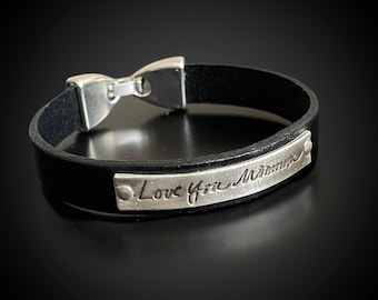 May include: Black leather bracelet with a silver clasp and a silver plate engraved with the words "Love you Momma". The bracelet is a simple, elegant design.