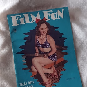 May include: A vintage "Film Fun" magazine cover featuring a woman in a polka-dot swimsuit. The cover is teal with the text "Film Fun" and "Polka-dots and Dash". The magazine is lying on a white textured surface.
