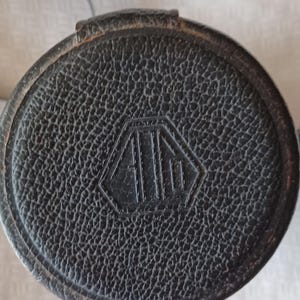 Puede incluir: Estuche de cuero negro para objetivo de c&aacute;mara con un logotipo en forma de diamante que dice "A.I.I."