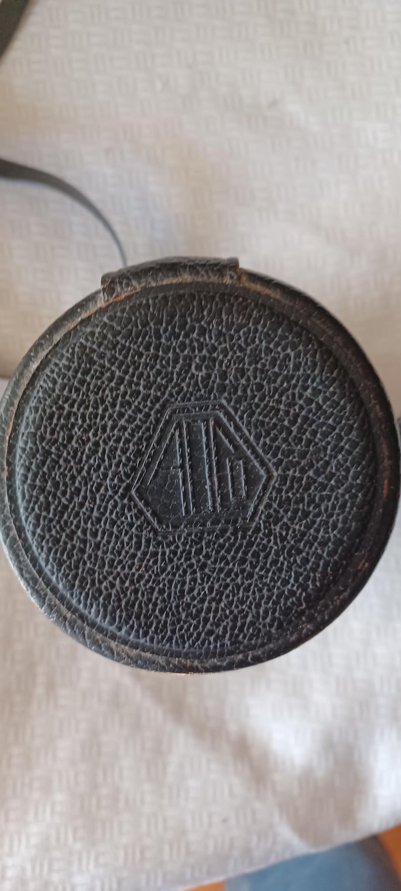 Puede incluir: Estuche de cuero negro para objetivo de c&aacute;mara con un logotipo en forma de diamante que dice "A.I.I."