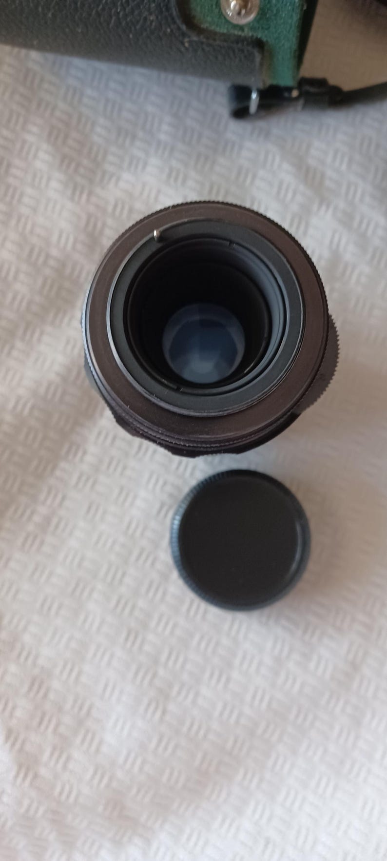 Puede incluir: Un objetivo de c&aacute;mara negro con un anillo plateado alrededor del borde. El objetivo est&aacute; sobre una superficie blanca con una tapa de objetivo negra al lado.