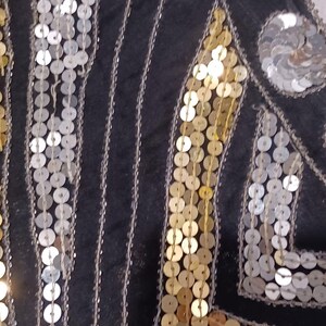 Puede incluir: Primer plano de una prenda negra adornada con lentejuelas plateadas y doradas. Las lentejuelas est&aacute;n dispuestas en patrones verticales y geom&eacute;tricos, creando un efecto brillante. El dise&ntilde;o sugiere un estilo vintage o formal.