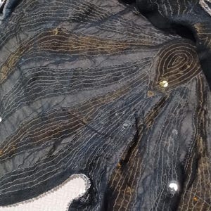 Puede incluir: Tela negra con un patr&oacute;n de l&iacute;neas curvas y lentejuelas. El borde superior tiene un dise&ntilde;o de lentejuelas doradas y plateadas en un patr&oacute;n de rayas. La tela est&aacute; drapeada sobre una superficie blanca.