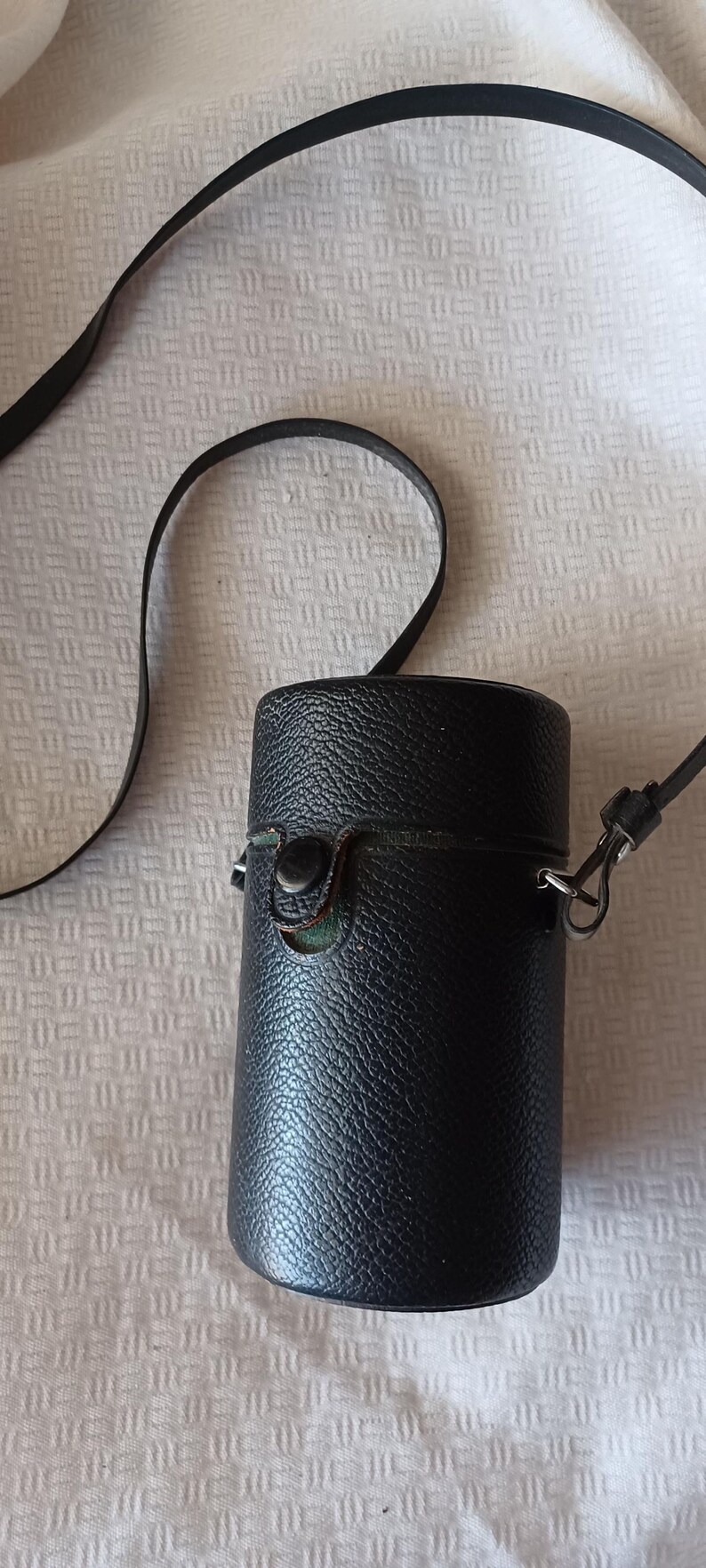 Puede incluir: Una funda de c&aacute;mara de cuero negro con una correa y un cierre de metal. La funda tiene una superficie texturizada.