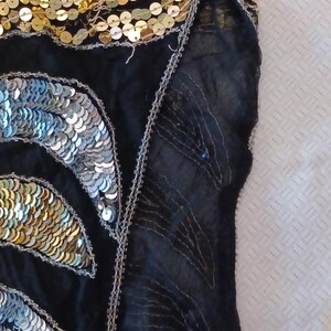 Puede incluir: Tela negra adornada con lentejuelas doradas y plateadas. Las lentejuelas est&aacute;n dispuestas en un patr&oacute;n similar a una hoja, con lentejuelas plateadas a la izquierda y doradas a la derecha. Los bordes est&aacute;n ribeteados con hilo plateado.