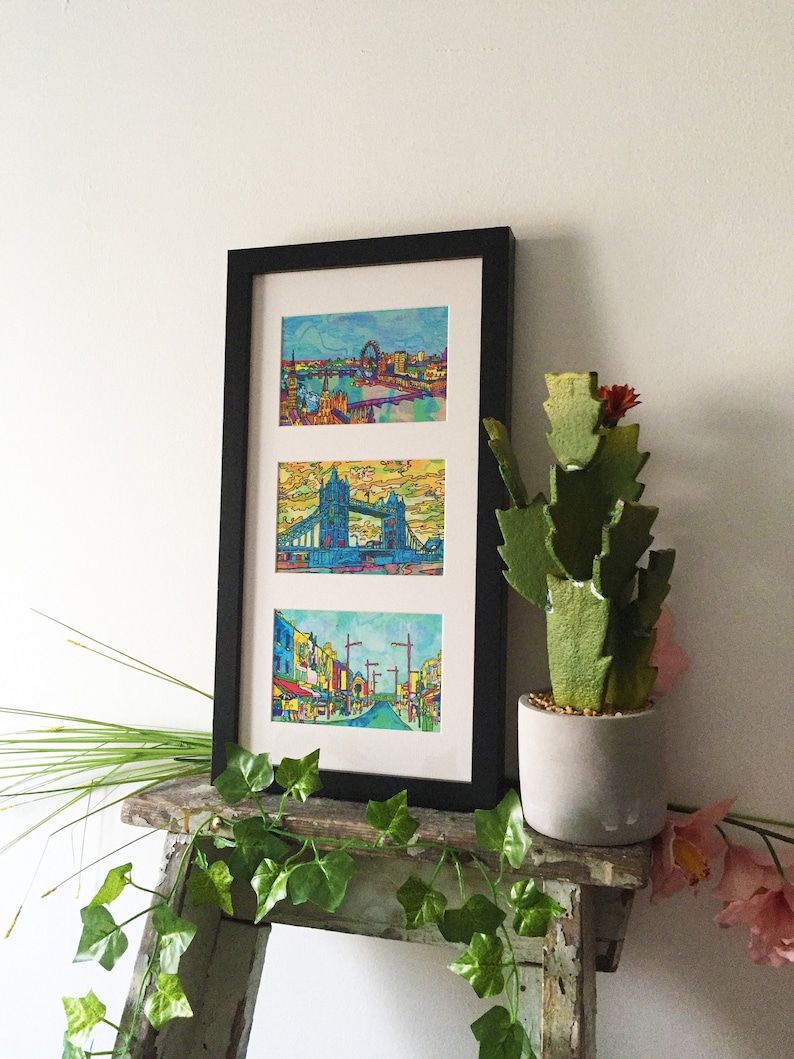 May include: A black framed print with three colorful images of London landmarks. The top image shows the London Eye, the middle image shows Tower Bridge, and the bottom image shows a street scene.