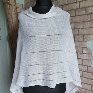 May include: White crochet poncho with a striped pattern. The poncho is displayed on a mannequin.