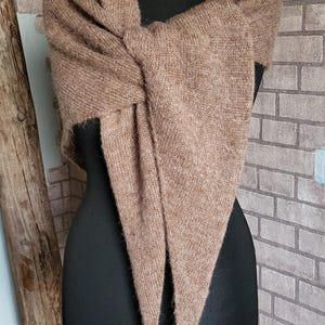 May include: A brown knitted shawl with a fringed edge. The shawl is draped over a black mannequin.