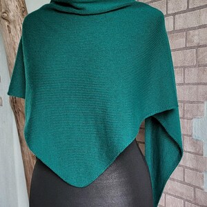 Könnte beinhalten: Ein türkisfarbener gestrickter Schal oder Poncho mit dreieckiger Form. Der Schal ist über eine schwarze Schaufensterpuppe gelegt.