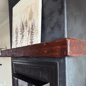May include: A black fireplace with a wood mantel and a painting of a snowy forest scene above it.