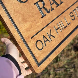 Close-up of custom wooden ranch sign showing thick Baltic birch layers and engraved lettering, personalized farm entrance sign held by hand with Oak Hill Ranch text.