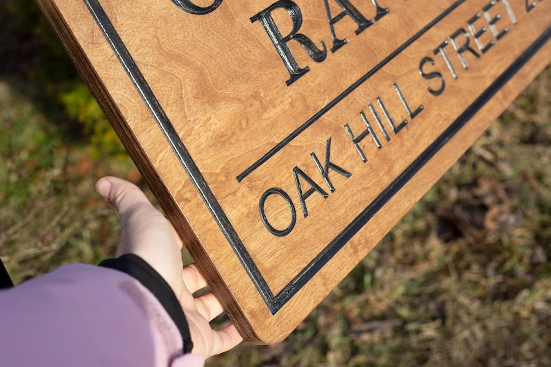 Close-up of custom wooden ranch sign showing thick Baltic birch layers and engraved lettering, personalized farm entrance sign held by hand with Oak Hill Ranch text.