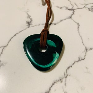 May include: A green and white swirl guitar pick pendant on a brown leather cord.