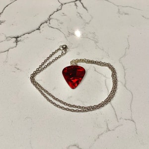 May include: A silver chain necklace with a red guitar pick pendant.