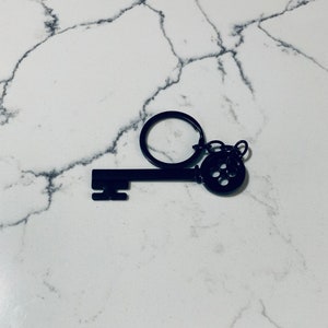 May include: Black metal key keychain with a decorative keyhole design. The key is attached to a silver ring.