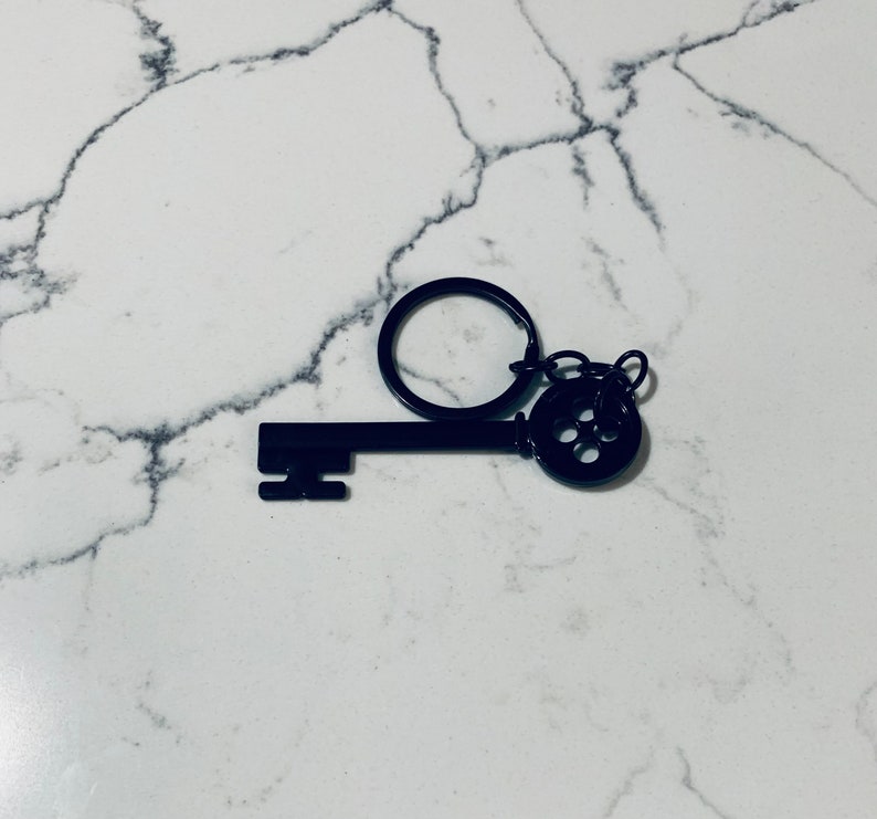 May include: Black metal key keychain with a decorative keyhole design. The key is attached to a silver ring.