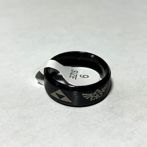 May include: A black ring with a silver Triforce and a silver winged design. The ring is size 9.