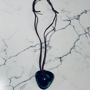May include: A dark green, triangular pendant with a hole in the center hangs from a brown leather cord. The pendant has a swirl pattern.