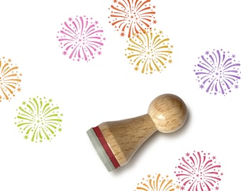 May include: A wooden rubber stamp with a red ink pad and a design of a firework. The stamp is used to create colorful firework designs on paper.