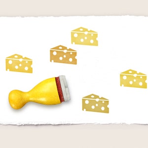 Könnte beinhalten: Ein gelber Stempel aus Gummi mit einem Holzgriff, der verwendet wird, um Bilder von Schweizer Käse zu erstellen. Der Stempel befindet sich auf einem weißen Papierhintergrund mit fünf Abdrücken des Käses.