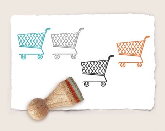 May include: Four rubber stamps with a shopping cart design. The stamps are in different colors: teal, gray, black, and orange. The stamps are on a white piece of paper with a rough texture.
