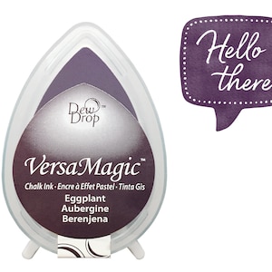 May include: A purple VersaMagic chalk ink pad in a teardrop shape with the words "Dew Drop" and "VersaMagic" on the front. The ink pad is labeled "Eggplant, Aubergine, Berenjena".