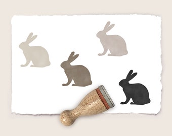 May include: A set of four rubber stamps featuring silhouettes of rabbits in different shades of brown and black. The stamps are mounted on wooden handles.