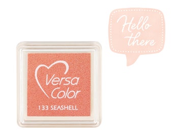 May include: A square, clear plastic container with a pink ink pad inside. The ink pad has a white heart with the words "Versa Color" and the number "133 SEASHELL" printed on it.