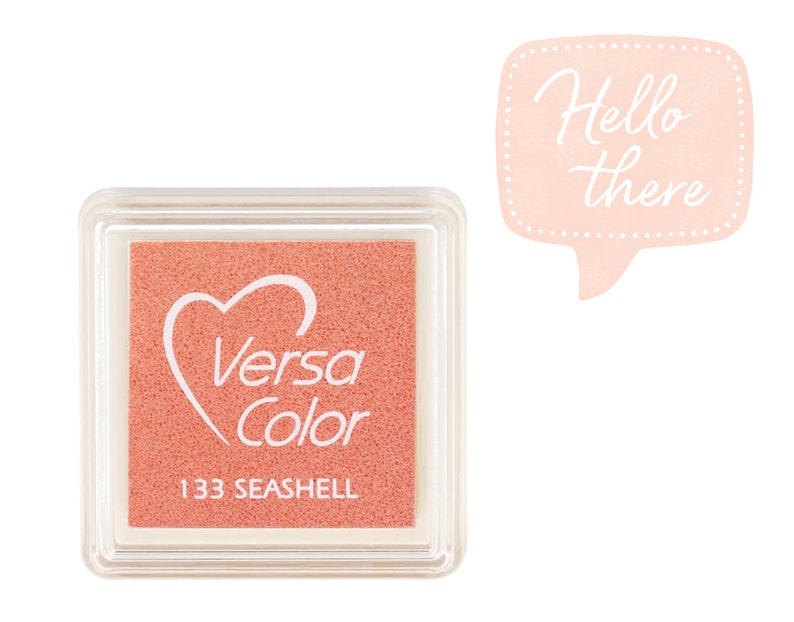 May include: A square, clear plastic container with a pink ink pad inside. The ink pad has a white heart with the words "Versa Color" and the number "133 SEASHELL" printed on it.