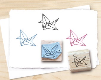 May include: Four wooden stamps with a geometric origami crane design. The stamps are in various colors, including black, blue, pink, and red. The stamps are on a white background.