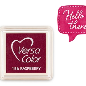 Könnte beinhalten: Ein quadratischer, transparenter Plastikbehälter mit einem roten Stempelkissen im Inneren. Das Stempelkissen hat ein weißes Herz mit den Worten "Versa Color" darin. Das Stempelkissen ist mit "156 Raspberry" beschriftet. Im Hintergrund befindet sich eine rosa Sprechblase mit weißen Punkten und den Worten "Hello there" in weißem Text.
