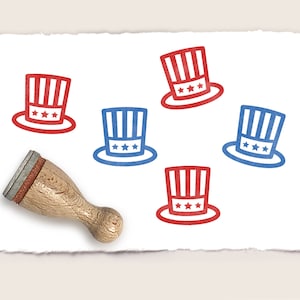 Könnte beinhalten: Fünf rot-weiß-blaue Onkel-Sam-Hüte mit Sternen auf weißem Hintergrund. Ein Holz-Stempel mit einem roten Gummiteil ist ebenfalls abgebildet.
