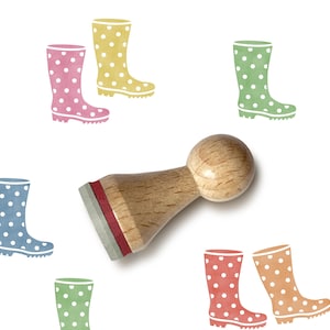 May include: A wooden stamp with a round handle and a red ink pad is surrounded by colourful illustrations of polka-dotted wellington boots. The boots are in various colours, including pink, yellow, green, and blue, on a white background.
