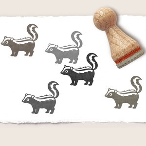 Könnte beinhalten: Ein Stempel aus Gummi mit einer Schwarzweißillustration eines Stinktiers. Der Stempel ist aus Holz und hat eine rot-weiße Basis.