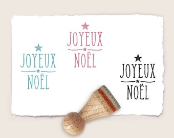 May include: Three rubber stamps with the text "Joyeux Noel" in different colors and fonts. The stamps are on a white background.