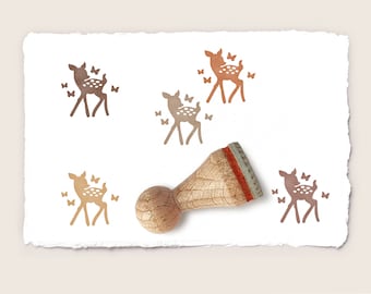 May include: A wooden stamp with a brown deer and butterflies design. The stamp is on a white paper background with several impressions of the deer and butterflies.