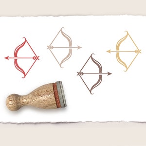 Puede incluir: Cuatro sellos de goma de diferentes colores con un diseño de arco y flecha. Los sellos están sobre un papel blanco con un mango de madera.