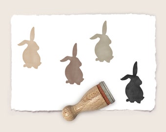 May include: A wooden stamp with a brown rubber pad featuring a silhouette of a rabbit. The stamp is used to create multiple impressions of the rabbit on a white paper background.