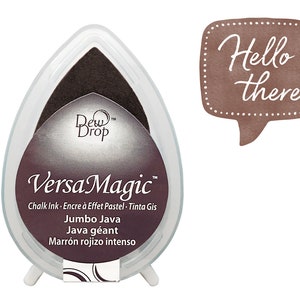 Könnte beinhalten: Ein braunes VersaMagic Jumbo Java Kreidetinte-Stempelkissen in einem transparenten Kunststoffgehäuse. Das Stempelkissen hat eine dunkelbraune Oberfläche. Eine braune Sprechblase mit den Worten "Hello there" befindet sich neben dem Stempelkissen.