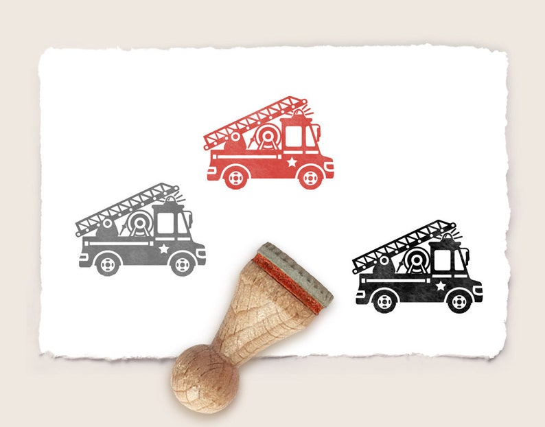 Puede incluir: Un sello de goma de madera con un dise&ntilde;o de cami&oacute;n de bomberos rojo y negro. El sello est&aacute; sobre un fondo blanco.