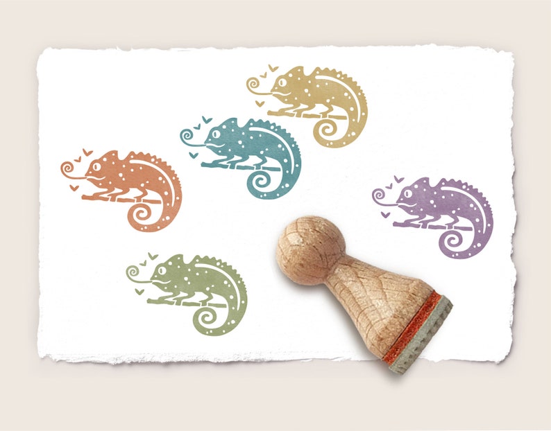 May include: Five colorful rubber stamps of a chameleon with a curled tail. The stamps are arranged in a circle around a wooden stamp handle. The chameleons are in shades of orange, blue, green, and purple.