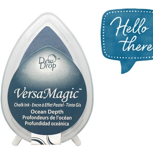 Könnte beinhalten: Ein blauer VersaMagic Kreidetinten-Stempel in einem tropfenförmigen Behälter. Die Tinte ist mit "Ocean Depth" beschriftet und enthält Text in mehreren Sprachen. Eine blaue Sprechblase mit den Worten "Hello there" ist ebenfalls vorhanden.
