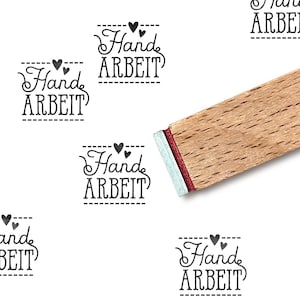 Pode incluir: Um carimbo de madeira com a palavra "Hand ARBEIT" em uma fonte decorativa, repetida em um fundo branco. O carimbo tem uma borda vermelha e prateada. A imagem sugere um tema artesanal ou feito &agrave; m&atilde;o.