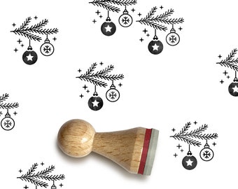 May include: A wooden rubber stamp with a design of a Christmas tree branch with ornaments. The stamp is on a white background.