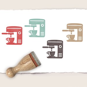 Può includere: Quattro timbri in gomma con diversi sfondi colorati che raffigurano una macchina per il caffè con una tazza di caffè. I timbri sono su uno sfondo di carta bianca. Un manico di timbro in legno si trova nell'angolo in basso a sinistra dell'immagine.