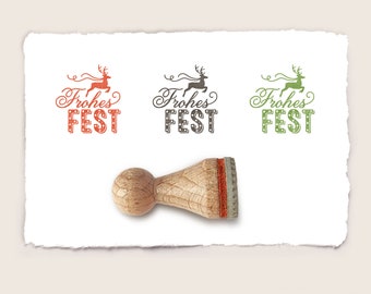 May include: A wooden stamp with a red reindeer and the text "Frohes Fest" in black. The stamp is on a white piece of paper with two other stamps, one with a green reindeer and the other with a brown reindeer.